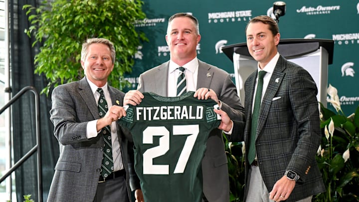 Michigan State football's new coach Pat Fitzgerald, center, holds up a jersey with MSU President Kevin Guskiewicz, left, and athletic director J Batt, right, during Fitzgerald's introductory press conference at the Tom Izzo Football Building in East Lansing.