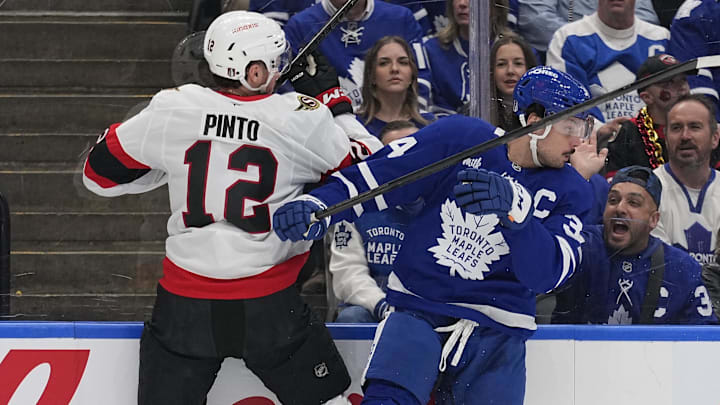 Apr 20, 2025; Toronto, Ontario, CAN; Toronto Maple Leafs forward Auston Matthews (34) checks Ottawa Senators forward Shane Pinto (12) along the boards during the first period of game one of the first round of the 2025 Stanley Cup Playoffs at Scotiabank Arena. Mandatory Credit: John E. Sokolowski-Imagn Images