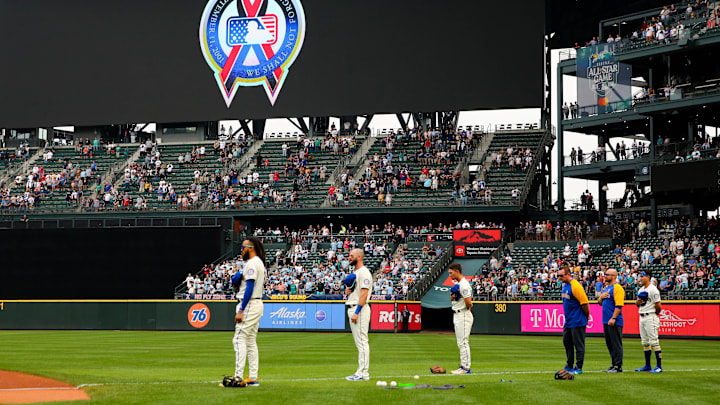 Sep 11, 2022; Seattle, Washington, USA;  An MLB logo with a graphic remembering the September 11th terrorist attacks is shown on the video screen as Seattle Mariners players hold their hats before the game against Atlanta Braves at T-Mobile Park. The Mariners beat the Braves 8-7. Mandatory Credit: Lindsey Wasson-Imagn Images