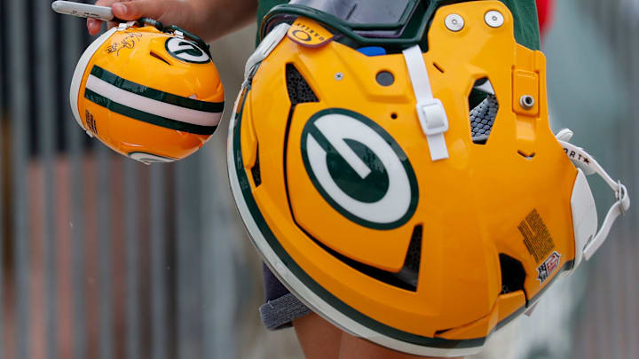 A fan carries an autographed mini helmet in one hand and Green Bay Packers offensive tackle Zach Tom’s helmet in the other.