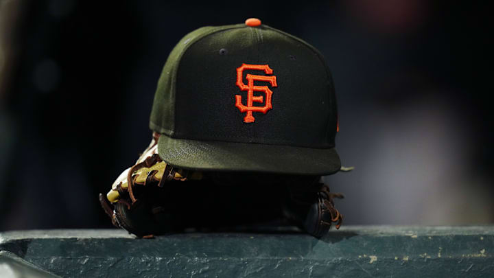 A San Francisco Giants cap sits on top of a glove which sits on a rail of a dugout. 