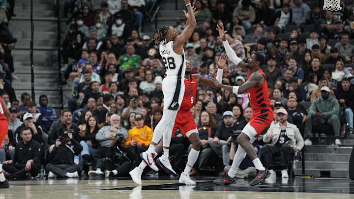 Dec 21, 2024; San Antonio, Texas, USA;  San Antonio Spurs center Charles Bassey (28) shoots the ball against Portland Trail Blazers forward Jerami Grant (9) and center Deandre Ayton (2) in the first half at Frost Bank Center. Mandatory Credit: Daniel Dunn-Imagn Images