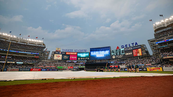 Jul 5, 2024; Bronx, New York, USA; A rain delay message is displayed on the main scoreboard as Yankees ground crew cover the field with a tarp. Mandatory Credit: Vincent Carchietta-USA TODAY Sports