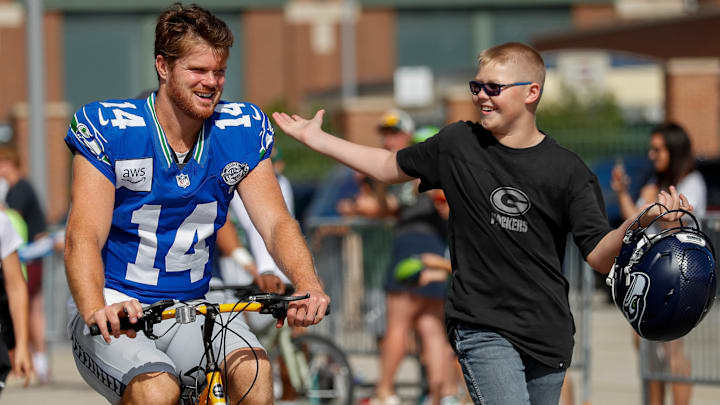 Seattle Seahawks quarterback Sam Darnold (14) shares a laugh with a fan as he rides a bicycle to a joint practice with the Green Bay Packers on Thursday, August 21, 2025, at Lambeau Field in Green Bay, Wis. 