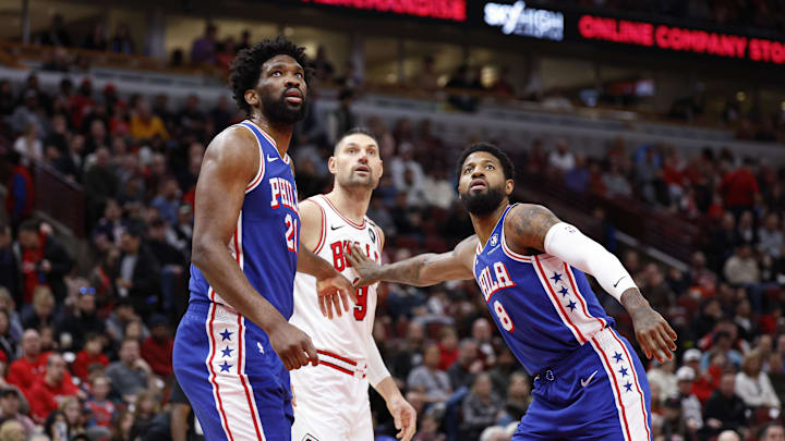Dec 8, 2024; Chicago, Illinois, USA; Philadelphia 76ers center Joel Embiid (21) and forward Paul George (8) defend against Chicago Bulls center Nikola Vucevic (9) during the first half at United Center. Mandatory Credit: Kamil Krzaczynski-Imagn Images