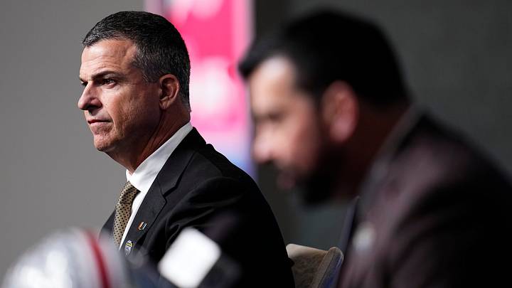 Miami (FL) Hurricanes head coach Mario Cristobal listens to Ohio State Buckeyes head coach Ryan Day talk to media during a Cotton Bowl press conference at AT&T Stadium in Arlington, Texas prior to their College Football Playoff quarterfinal matchup on Dec. 30, 2025.