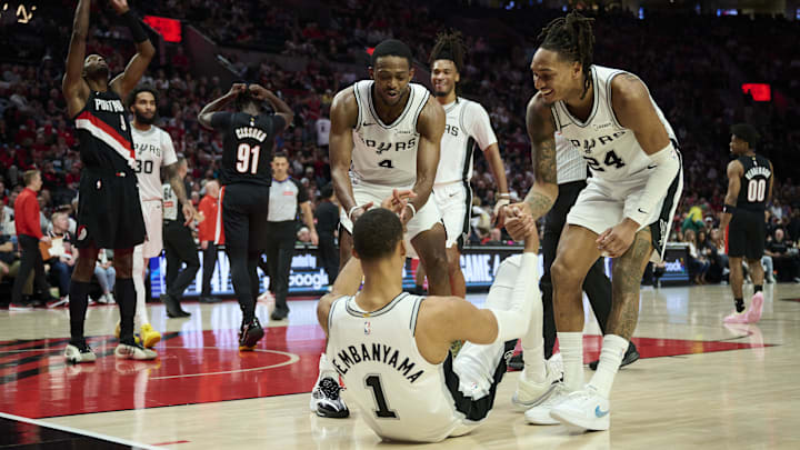 Apr 26, 2026; Portland, Oregon, USA; San Antonio Spurs guard De'aaron Fox (4) and guard Devin Vassell (24) help forward Victor Wembanyama (1) off the court during the second half against the Portland Trail Blazers during game four of the first round of the 2026 NBA Playoffs at Moda Center. Mandatory Credit: Troy Wayrynen-Imagn Images