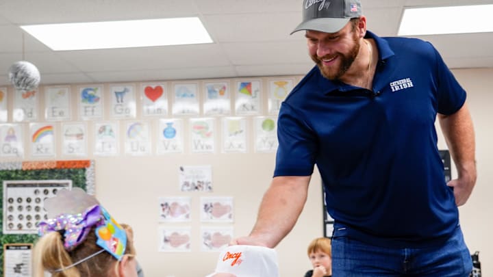 Cincinnati Bengals center Ted Karras (64), right, hands a kindergartener from Maggie Adams    class a hat for her birthday on Tuesday, Nov. 28, 2023, at St. Joseph   s Consolidated School in Hamilton, Ohio. Over a year ago Karras began selling The Cincy Hat, a project that gives 100% of the proceeds from hat sales to The Village of Merici, an Indianapolis-based    living community and services provider for adults with disabilities.   