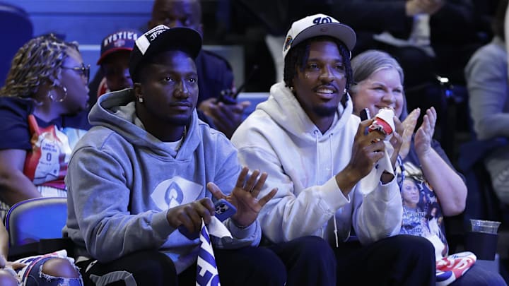 May 16, 2025; Washington, District of Columbia, USA; Washington Commanders wide receiver Deebo Samuels (L) and Commanders quarterback Jayden Daniels (R) wave to the crowd from courts wide during the game between the Washington Mystics and Atlanta Dream at CareFirst Arena. Mandatory Credit: Geoff Burke-Imagn Images