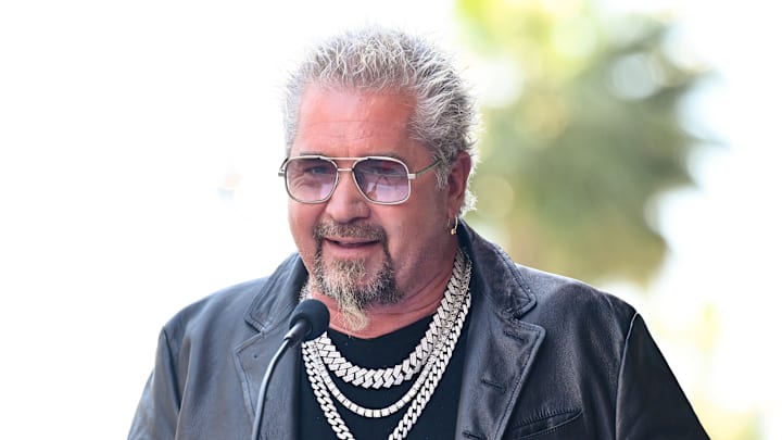 Guy Fieri speaking at a microphone while wearing a leather jacket