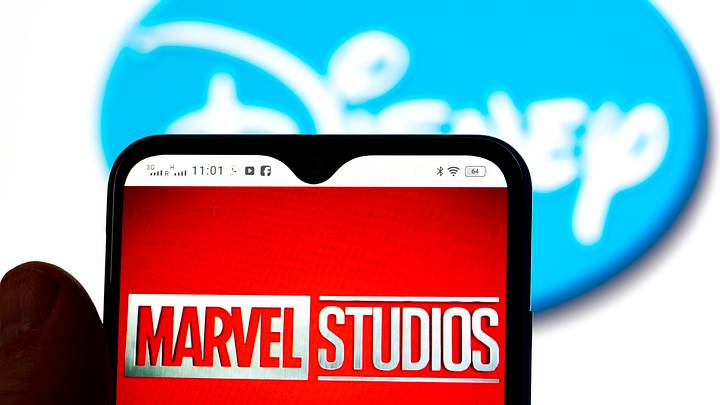In this photo illustration, the Marvel Studios logo is seen displayed on a smartphone screen with a Disney logo in the background