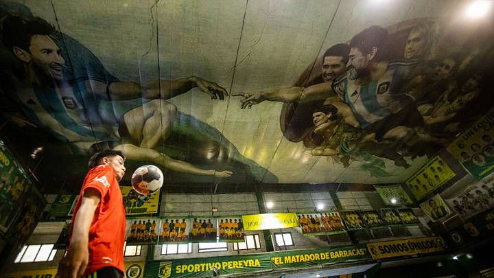 Un hombre juega al fútbol en el club Sportivo Pereyra, bajo un mural que retrata a Diego Maradona y Lionel Messi Un hombre juega al fútbol en el club Sportivo Pereyra, bajo un mural que retrata a Diego Maradona y Lionel Messi