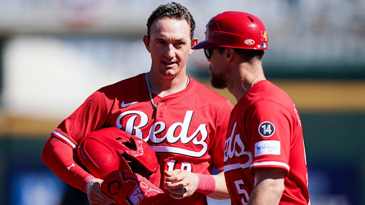 Cincinnati Reds outfielder Austin Hays (12), left, speaks with first base coach Collin Cowgill (54) in the first inning of a Cactus League game between the Cincinnati Reds and Cleveland Guardians, Saturday, Feb. 22, 2025, at the Goodyear Ballpark in Goodyear, Ariz.