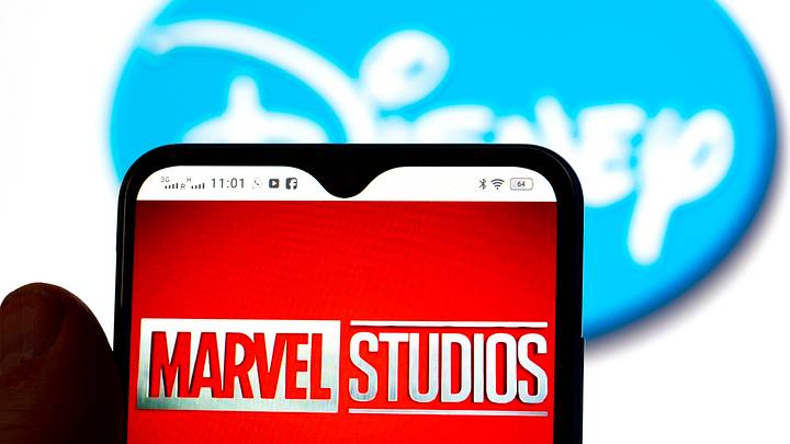 In this photo illustration, the Marvel Studios logo is seen displayed on a smartphone screen with a Disney logo in the background