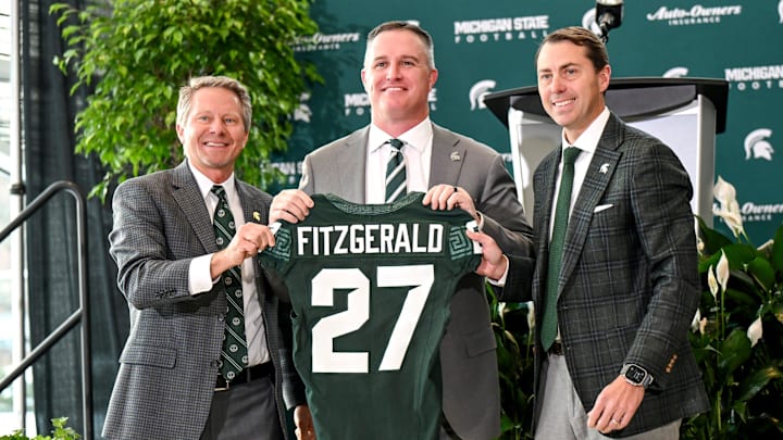 Michigan State football's new coach Pat Fitzgerald, center, holds up a jersey with MSU president Kevin Guskiewicz, left, and athletic director J Batt, right, during Fitzgerald's introductory press conference on Tuesday, Dec. 2, 2025, at the Tom Izzo Football Building in East Lansing.