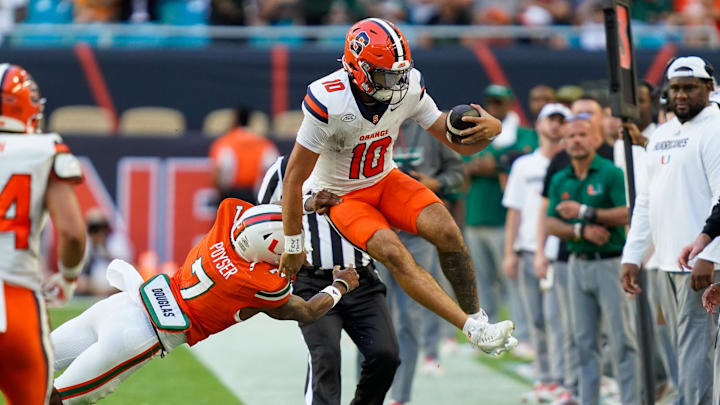 Nov 8, 2025; Miami Gardens, Florida, USA; Syracuse Orange quarterback Rickie Collins (10) leaps to avoid the tackle of Miami Hurricanes safety Zechariah Poyser (7) during the second quarter at Hard Rock Stadium. Mandatory Credit: Jeff Romance-Imagn Images