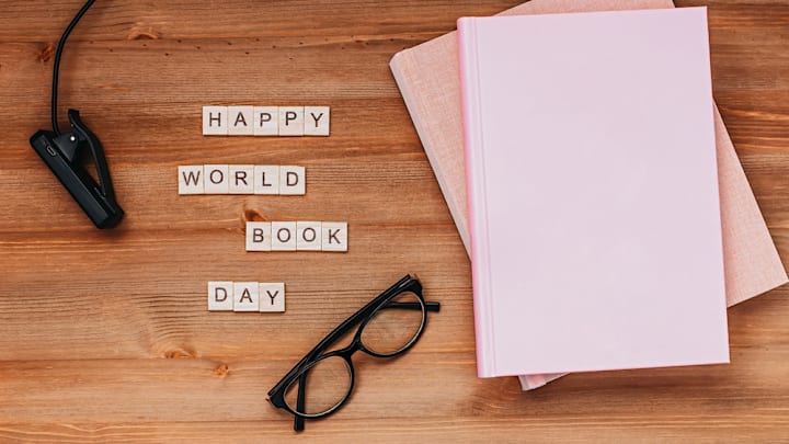 Books, glasses, and light along with "happy world book day" spelled out in Scrabble letters on a wooden background
