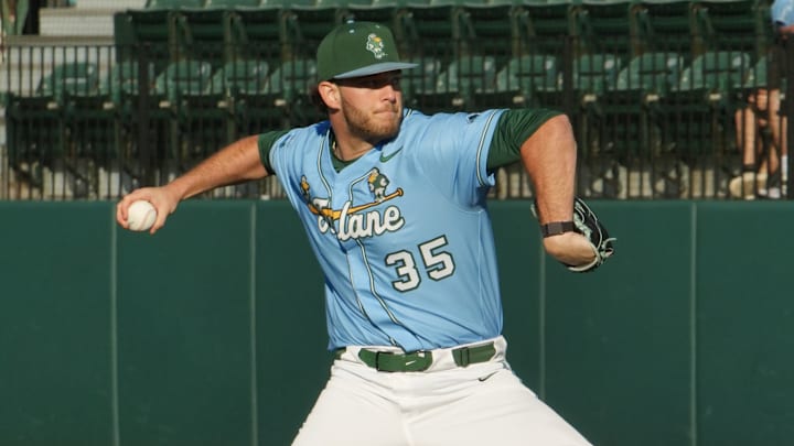 Pitcher winds up to throw baseball wearing green hat, blue jersey with number 35 and Tulane logo and white pants.