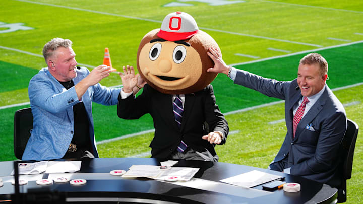 Jan 1, 2025; Pasadena, California, USA; Lee Corso (center) wears a Buckeyes mascot head  as Pat McAfee (left) and Kirk Herbstreit (right) watch at Rose Bowl Stadium. Mandatory Credit: Kirby Lee-Imagn Images