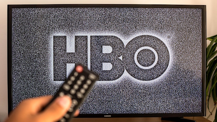 SPAIN - 2021/07/13: In this photo illustration a close-up of a hand holding a TV remote control seen displayed in front of the HBO logo on a tv in the background