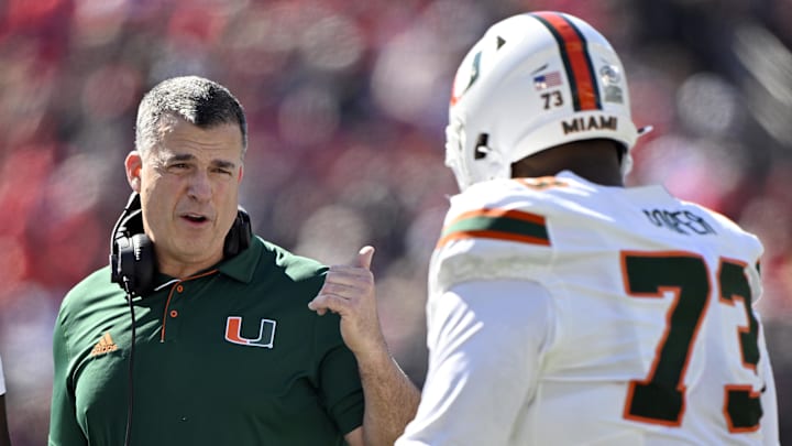Oct 19, 2024; Louisville, Kentucky, USA; Miami Hurricanes head coach Mario Cristobal talks with offensive lineman Anez Cooper (73) during the first half against the Louisville Cardinals at L&N Federal Credit Union Stadium. Mandatory Credit: Jamie Rhodes-Imagn Images