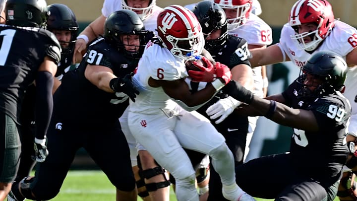 Nov 2, 2024; East Lansing, Michigan, USA; Indiana Hoosiers running back Justice Ellison (6) gets tackled by Michigan State Spartans defensive linemen Alex VanSumeren (91), Maverick Hansen (97) and Quindarius Dunnigan (99) during the first quarter at Spartan Stadium. Mandatory Credit: Dale Young-Imagn Images