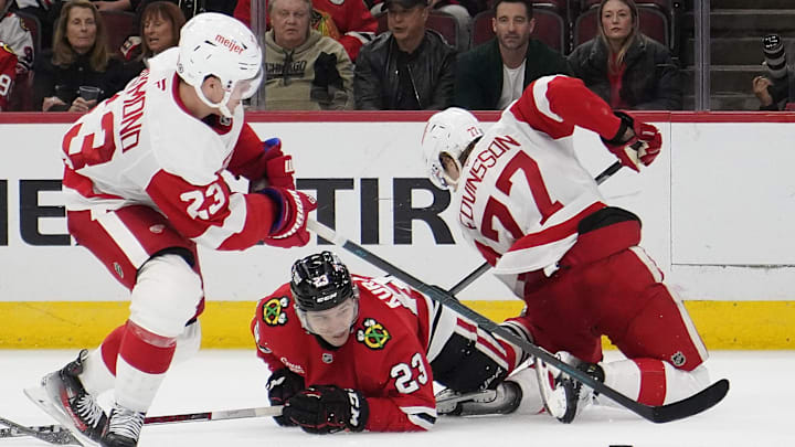 Nov 6, 2024; Chicago, Illinois, USA; Detroit Red Wings left wing Lucas Raymond (23) defenseman Simon Edvinsson (77)  and Chicago Blackhawks center Philipp Kurashev (23) go for the puck during the third period at United Center. Mandatory Credit: David Banks-Imagn Images
