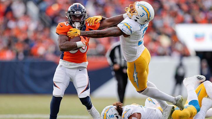 Dec 31, 2023; Denver, Colorado, USA; Denver Broncos running back Javonte Williams (33) stiff arms Los Angeles Chargers safety Derwin James Jr. (3) as linebacker Eric Kendricks (6) slides on the ground in the first quarter at Empower Field at Mile High.