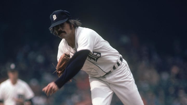 Former Detroit TIgers pitcher John Hiller throws a pitch wearing a white jersey and navy blue hat.
