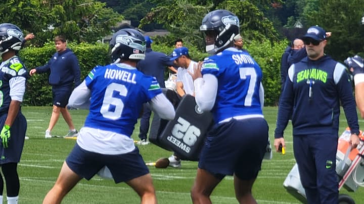 Seahawks offensive coordinator Ryan Grubb watches as quarterbacks Geno Smith and Sam Howell prepare to throw during a team drill at OTAs. Seahawks offensive coordinator Ryan Grubb watches as quarterbacks Geno Smith and Sam Howell prepare to throw during a team drill at OTAs.
