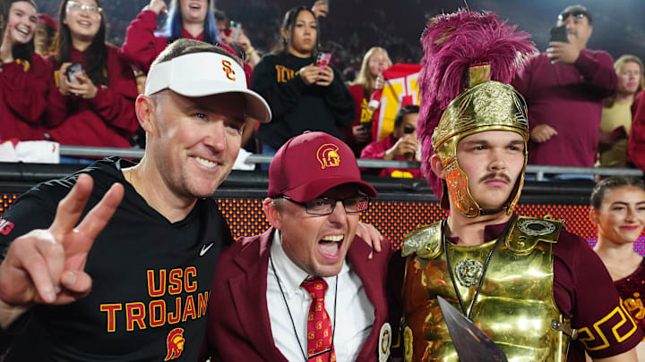 Nov 29, 2025; Los Angeles, California, USA; Southern California Trojans head coach Lincoln Riley (left) poses with Spirit of Troy marching band director James Vogel (center) and mascot Tommy Trojan after the game against the UCLA Bruins at United Airlines Field at Los Angeles Memorial Coliseum. Mandatory Credit: Kirby Lee-Imagn Images