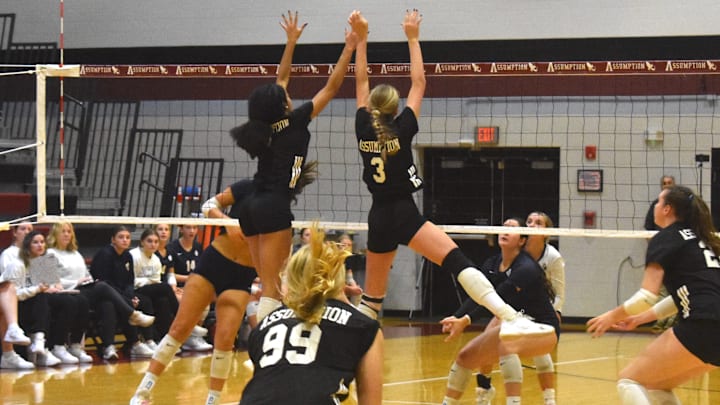 Assumption High School sophomores McKenzie Taylor, left, and Julie Lee successfully execute a block Tuesday, Oct. 14, 2025 in a victory against Notre Dame Academy while sophomore teammate Brooke Codey (99) looks on from her defensive specialist position. 