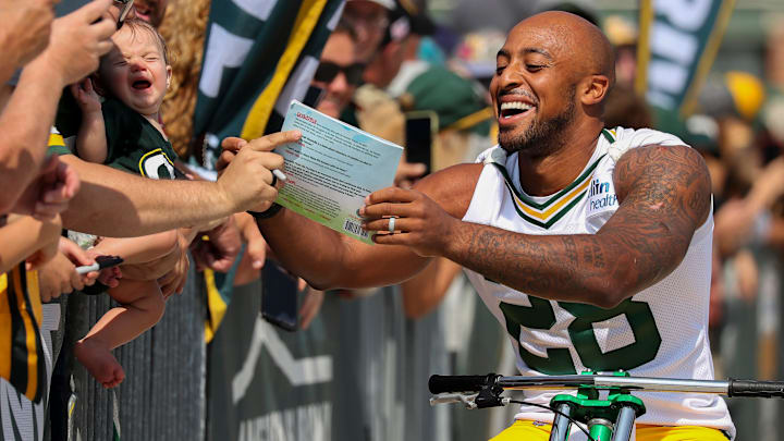Green Bay Packers running back AJ Dillon signs a copy of his children's book for a fan as he rides a bicycle to practice in the Dream Drive during the first day of training camp on Monday, July 22, 2024, at Lambeau Field in Green Bay, Wis.