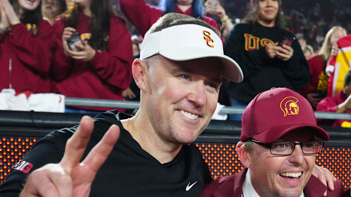 Nov 29, 2025; Los Angeles, California, USA; Southern California Trojans head coach Lincoln Riley (left) poses with Spirit of Troy marching band director James Vogel (center) and mascot Tommy Trojan after the game against the UCLA Bruins at United Airlines Field at Los Angeles Memorial Coliseum. Mandatory Credit: Kirby Lee-Imagn Images Nov 29, 2025; Los Angeles, California, USA; Southern California Trojans head coach Lincoln Riley (left) poses with Spirit of Troy marching band director James Vogel (center) and mascot Tommy Trojan after the game against the UCLA Bruins at United Airlines Field at Los Angeles Memorial Coliseum. Mandatory Credit: Kirby Lee-Imagn Images