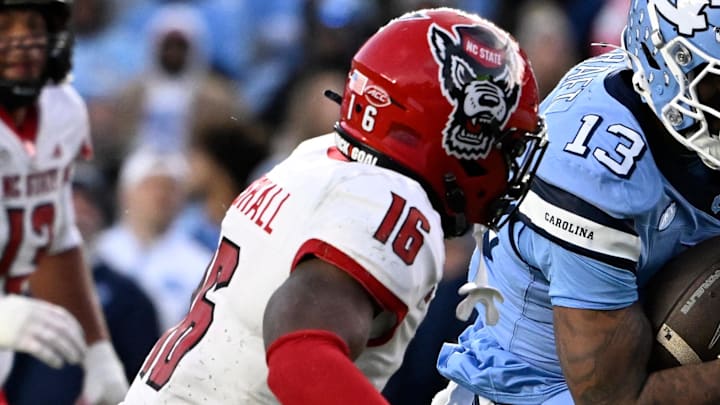 Nov 30, 2024; Chapel Hill, North Carolina, USA; North Carolina Tar Heels wide receiver J.J. Jones (13) scores a touchdown as North Carolina State Wolfpack cornerback Devon Marshall (16) and linebacker Sean Brown (0) defend in the second quarter at Kenan Memorial Stadium. Mandatory Credit: Bob Donnan-Imagn Images Nov 30, 2024; Chapel Hill, North Carolina, USA; North Carolina Tar Heels wide receiver J.J. Jones (13) scores a touchdown as North Carolina State Wolfpack cornerback Devon Marshall (16) and linebacker Sean Brown (0) defend in the second quarter at Kenan Memorial Stadium. Mandatory Credit: Bob Donnan-Imagn Images