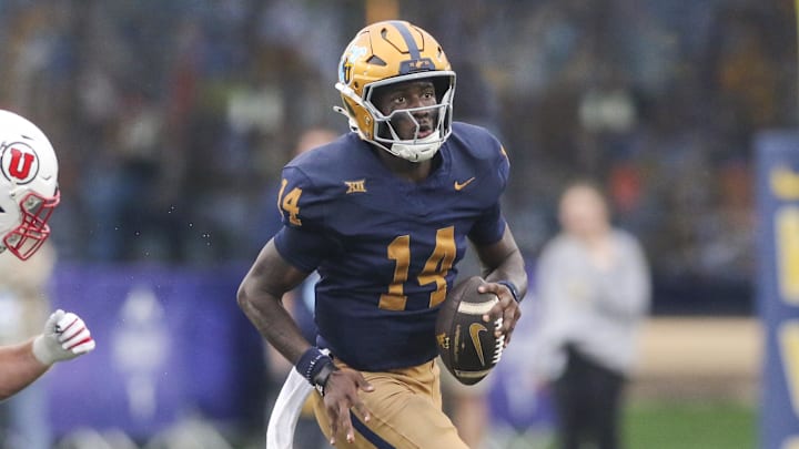 Sep 27, 2025; Morgantown, West Virginia, USA; West Virginia Mountaineers quarterback Khalil Wilkins (14) runs away from Utah Utes defensive end John Henry Daley (90) during the third quarter at Milan Puskar Stadium. Mandatory Credit: Ben Queen-Imagn Images