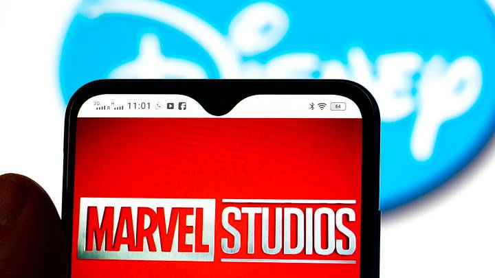 In this photo illustration, the Marvel Studios logo is seen displayed on a smartphone screen with a Disney logo in the background
