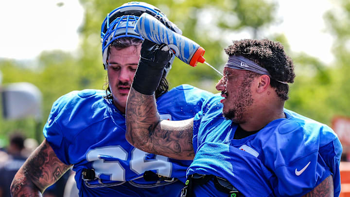 Detroit Lions guard Christian Mahogany squirts water in his face alongside guard Tate Ratledge at training camp