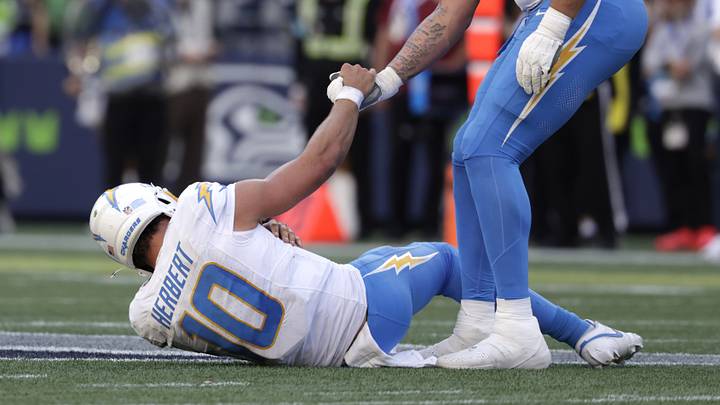 Oct 4, 2026; Seattle, Washington, USA;  Los Angeles Chargers offensive tackle Travis Burke (77) helps Los Angeles Chargers quarterback Justin Herbert (10) to his feet against the Seattle Seahawks during the second half at Lumen Field.  Mandatory Credit: Joe Nicholson-Imagn Images