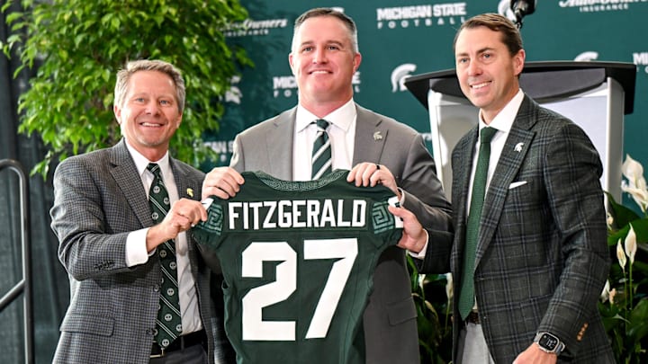 Michigan State football's new coach Pat Fitzgerald, center, holds up a jersey with MSU president Kevin Guskiewicz, left, and athletic director J Batt, right, during Fitzgerald's introductory press conference on Tuesday, Dec. 2, 2025, at the Tom Izzo Football Building in East Lansing.