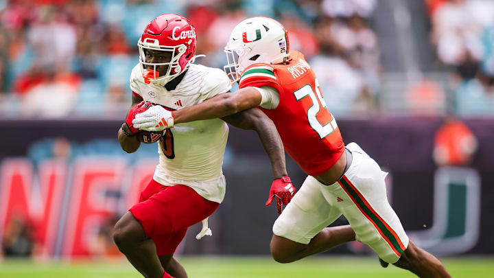 Nov 18, 2023; Miami Gardens, Florida, USA; Louisville Cardinals wide receiver Chris Bell (0) breaks a tackle attempt from Miami Hurricanes defensive back Jadais Richard (25) during the second quarter at Hard Rock Stadium. Mandatory Credit: Sam Navarro-Imagn Images