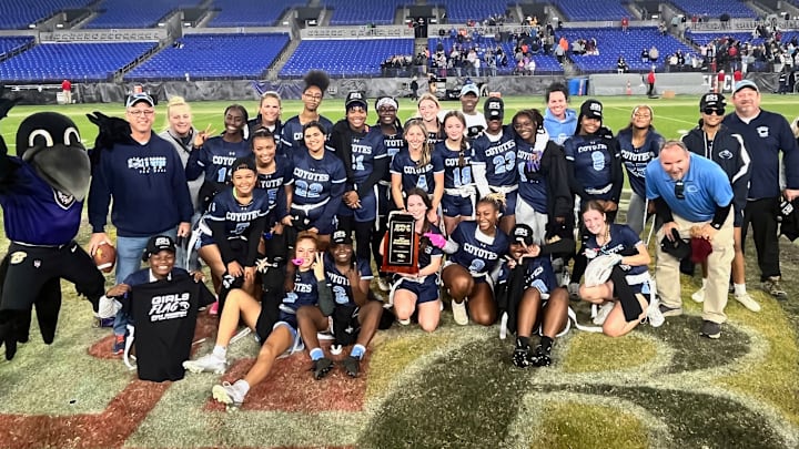 The Baltimore Ravens mascot joins the players and coaches of the Clarksburg girls flag football team, on the turf of M&T Bank Stadium, after the Coyotes won the Maryland state girls flag football championship on Friday.