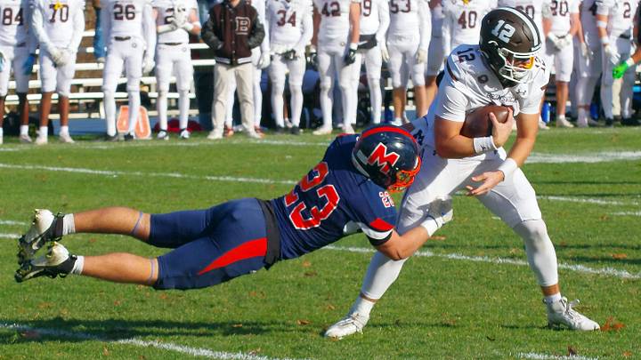 Dionisios Kitsos (23) of Milton Academy attempts to bring down Brunswick quarterback Ben Rolapp, but Rolapp broke away for a big gain in the 2025 matchup between the two teams. Dionisios Kitsos (23) of Milton Academy attempts to bring down Brunswick quarterback Ben Rolapp, but Rolapp broke away for a big gain in the 2025 matchup between the two teams.