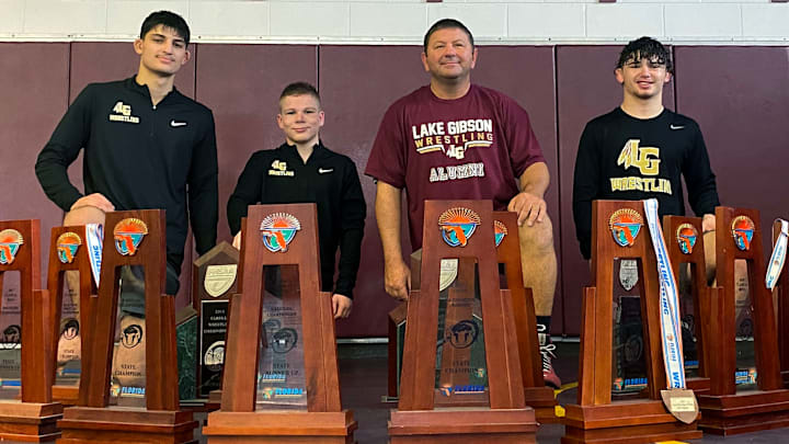 Sam Mustafo, RJ Felon, Coach Danny Walker and Christian Fretwell kneel around 15 Class 2A state championship and state runner-up trophies won by Lake Gibson. Winning a 2A state championship will be much harder this year with Somerset Academy and Jensen Beach joining the classification. All three wrestlers will be competing at the Walsh Jesuit Ironman tournament in Ohio this weekend. Sam Mustafo, RJ Felon, Coach Danny Walker and Christian Fretwell kneel around 15 Class 2A state championship and state runner-up trophies won by Lake Gibson. Winning a 2A state championship will be much harder this year with Somerset Academy and Jensen Beach joining the classification. All three wrestlers will be competing at the Walsh Jesuit Ironman tournament in Ohio this weekend.