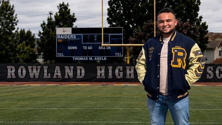 Rowland High junior offensive lineman Ethan De Anda stands on the Raiders' football field wearing a letterman jacket. De Anda founded the Ethan De Anda Letterman Legacy Foundation to help student-athletes who have earned varsity letters but cannot afford their own jackets.