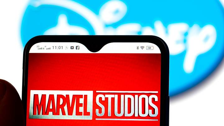 In this photo illustration, the Marvel Studios logo is seen displayed on a smartphone screen with a Disney logo in the background