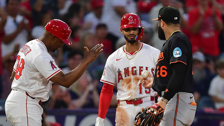 Angels left fielder Matthew Lugo (15) is handed the ball by Baltimore Orioles third baseman Emmanuel Rivera (26) after hitting an RBI triple for his first major league hit during the fourth inning at Angel Stadium. Mandatory Credit: Gary A. Vasquez-Imagn Images