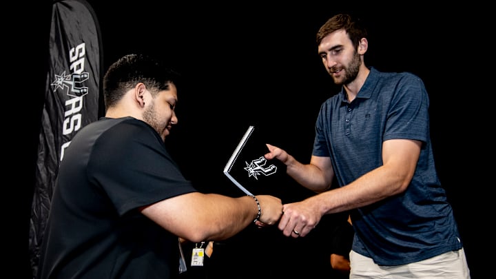 Aug 10, 2025; San Antonio, Texas, USA; San Antonio Spurs center Luke Kornet (7) hands out a notebook to a family during the team's fourth annual Back to School Bash at Frost Bank Center.