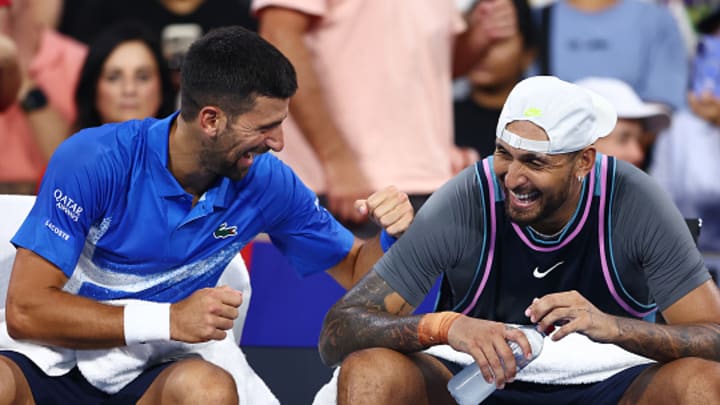 Novak Djokovic and Nick Kyrgios laugh on the bench during a double match.