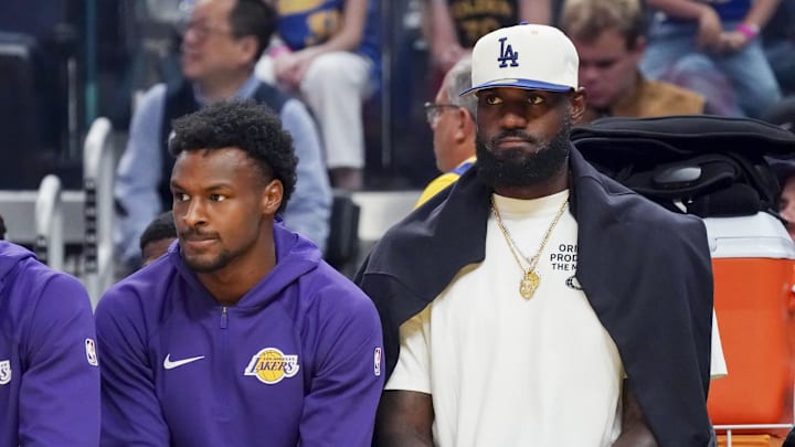 Oct 5, 2025; San Francisco, California, USA; Los Angeles Lakers guard Bronny James (9) and forward LeBron James (23), wearing a Los Angeles Dodgers cap, watch the action against the Golden State Warriors in the first quarter at Chase Center. Mandatory Credit: David Gonzales-Imagn Images Oct 5, 2025; San Francisco, California, USA; Los Angeles Lakers guard Bronny James (9) and forward LeBron James (23), wearing a Los Angeles Dodgers cap, watch the action against the Golden State Warriors in the first quarter at Chase Center. Mandatory Credit: David Gonzales-Imagn Images